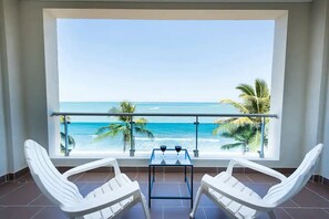 A balcony with two white chairs, a small table, and a view of the ocean. - Beautiful Beachfront Condo (Cabarete)