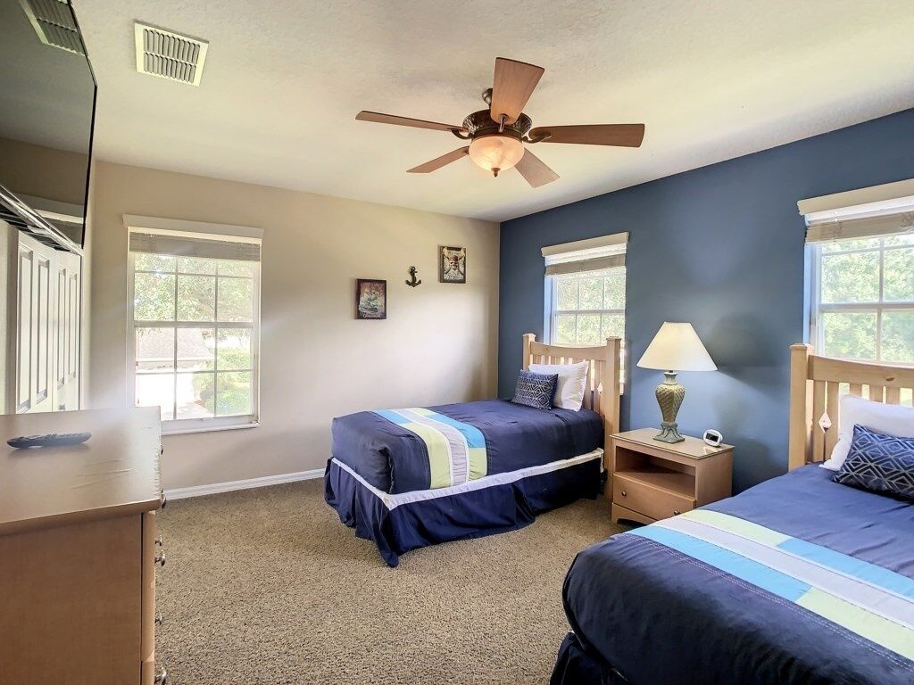 A bedroom with two beds, a ceiling fan, and a nightstand with a lamp.