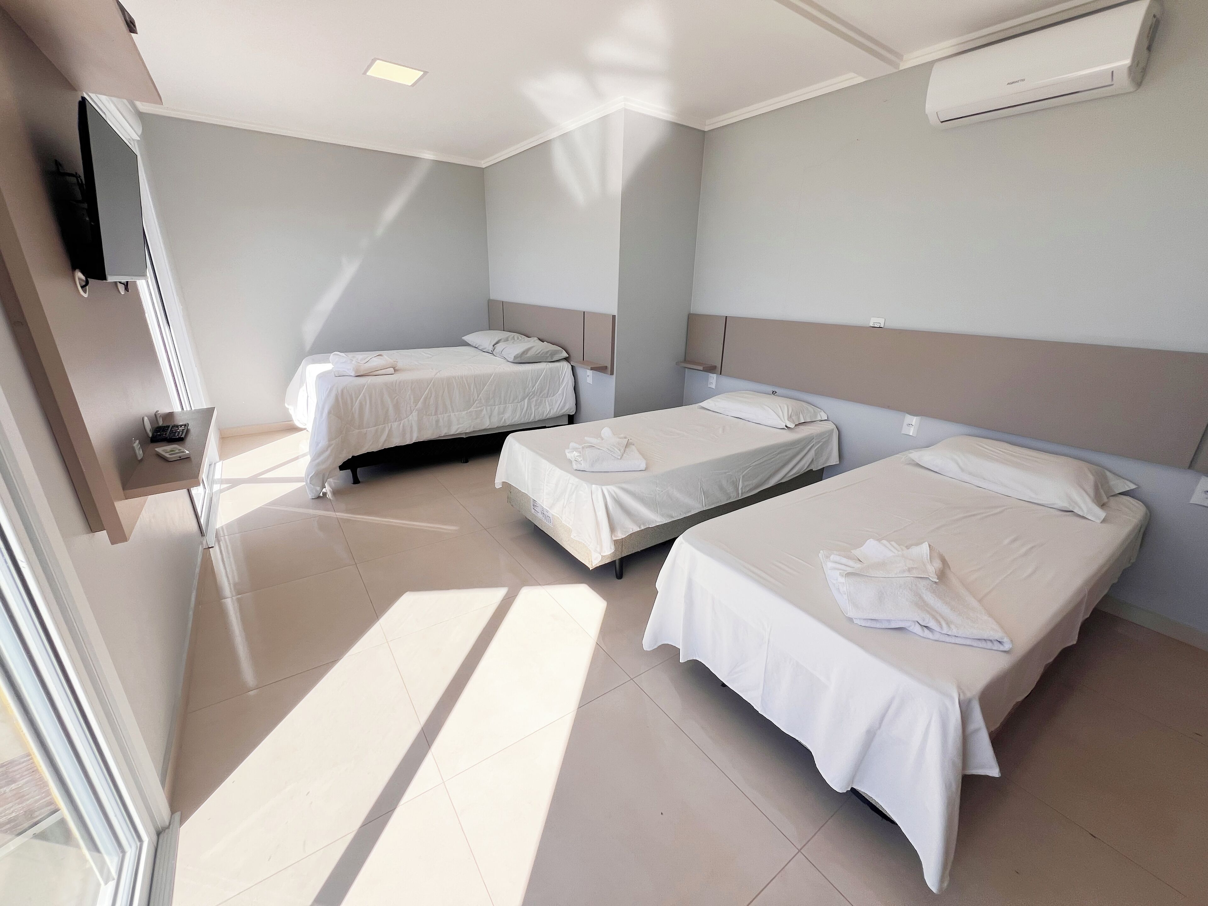 A hotel room with two beds, a flat-screen TV mounted on the wall, and a window providing natural light.
