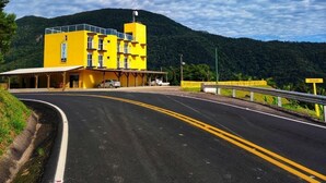 A yellow hotel building with a flat roof and multiple windows, surrounded by a road and greenery.