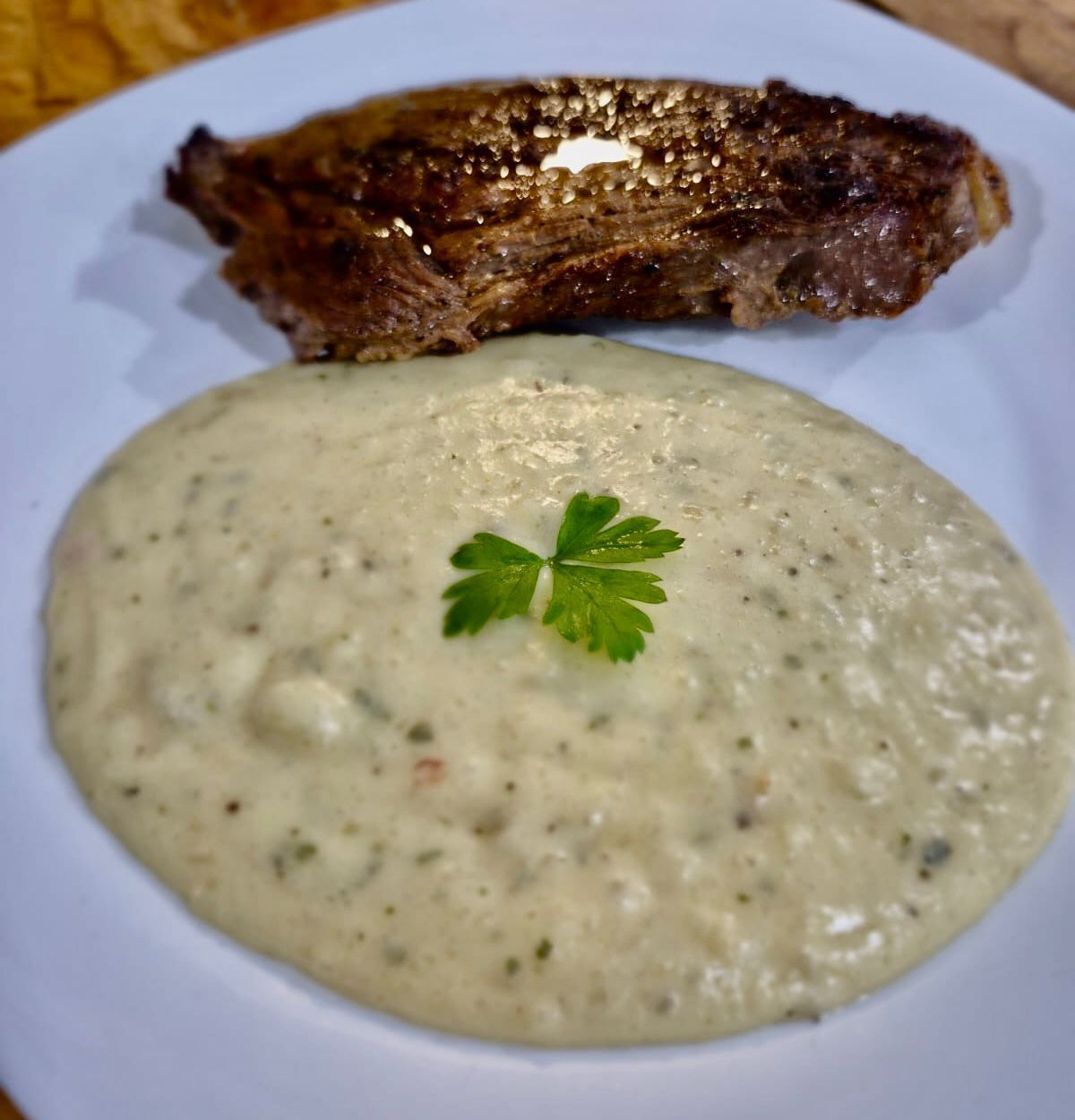 Un plato con un bistec a la parrilla y salsa cremosa adornado con perejil.