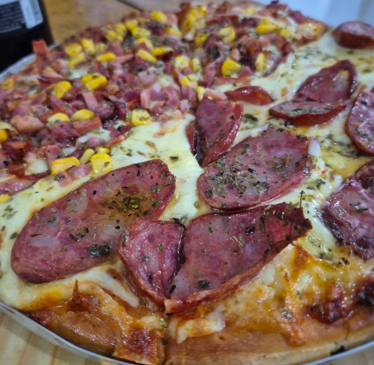 Una pizza con pepperoni y maíz sobre un plato blanco.