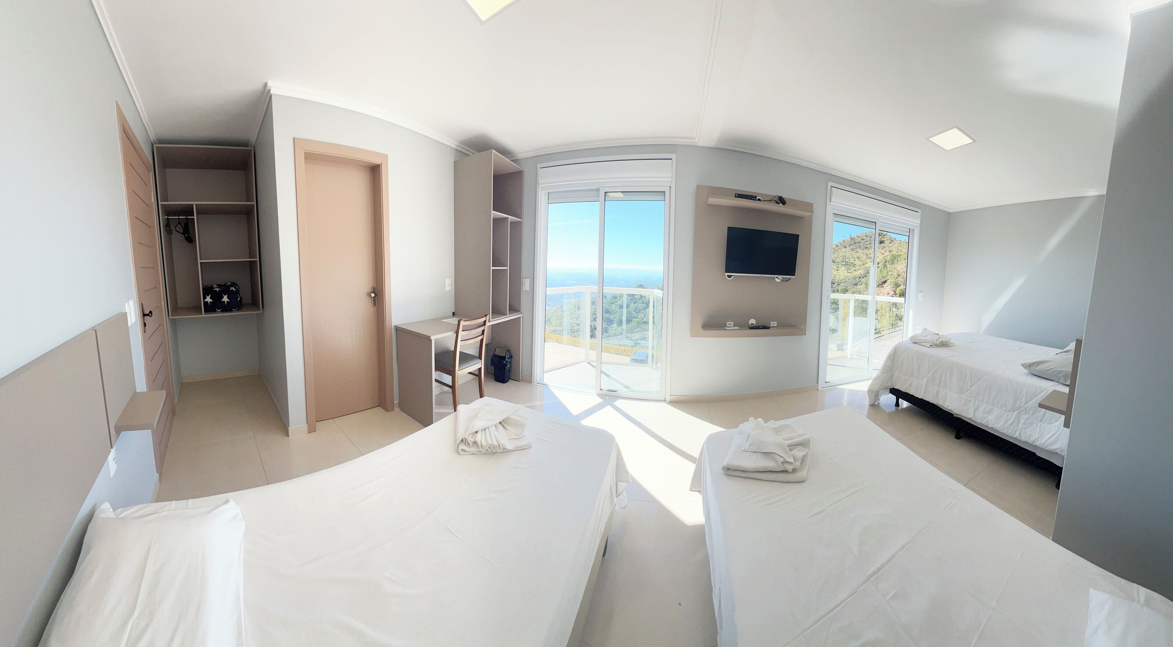 Quarto de hotel com duas camas, uma escrivaninha, uma cadeira, televisão e varanda com vista.