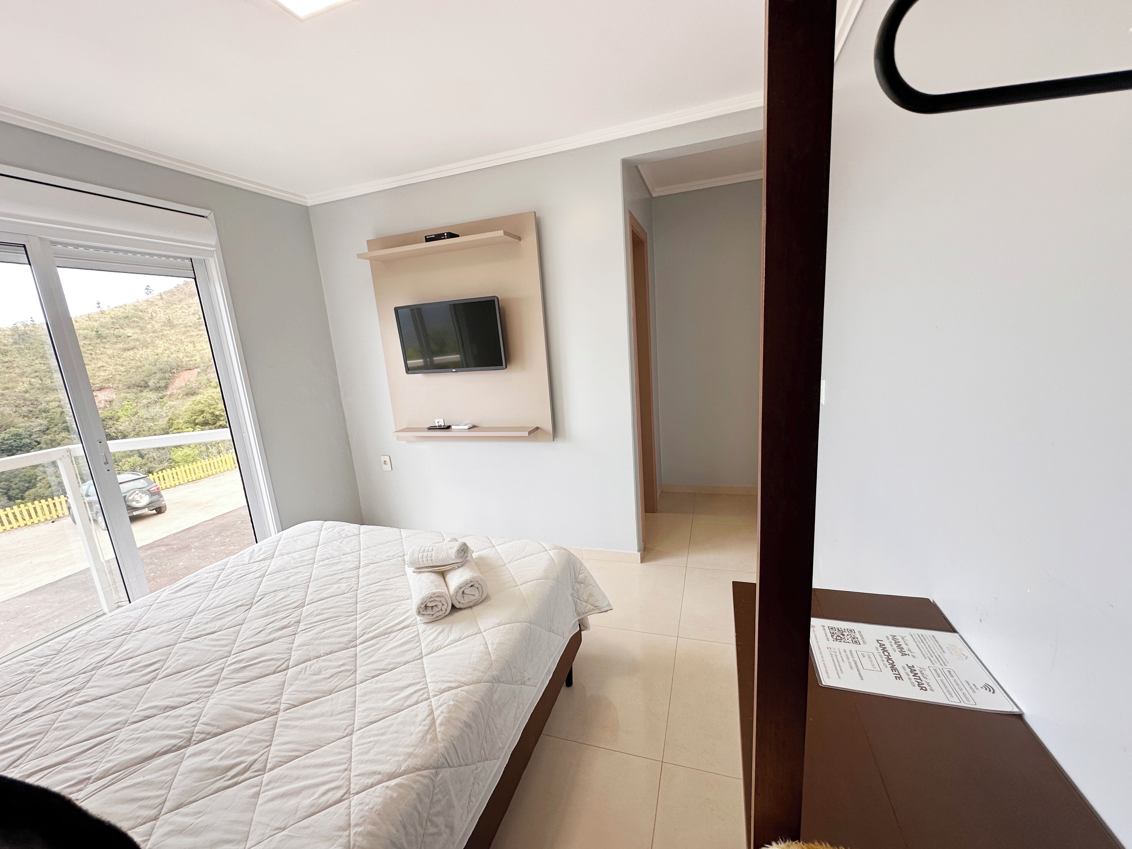 Habitación de hotel con cama, televisor montado en la pared y balcón con vistas al exterior.