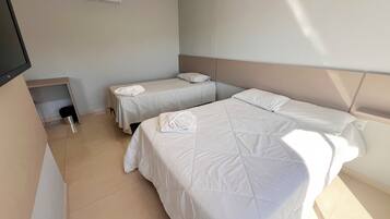 A hotel room with two beds, a small table, an air conditioning unit, and a TV mounted on the wall.