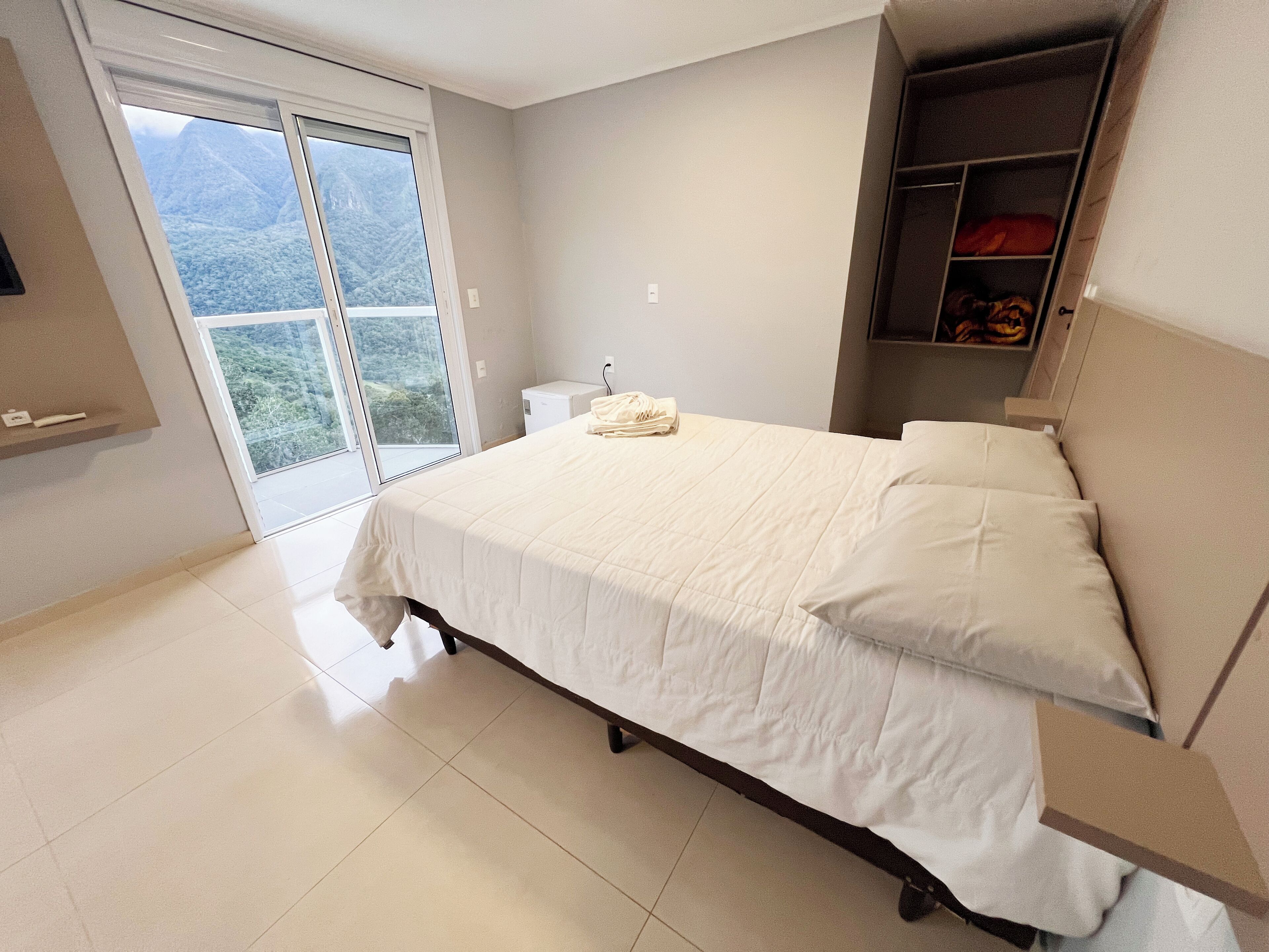 A bedroom with a large bed, a wardrobe, and a sliding glass door leading to a balcony.