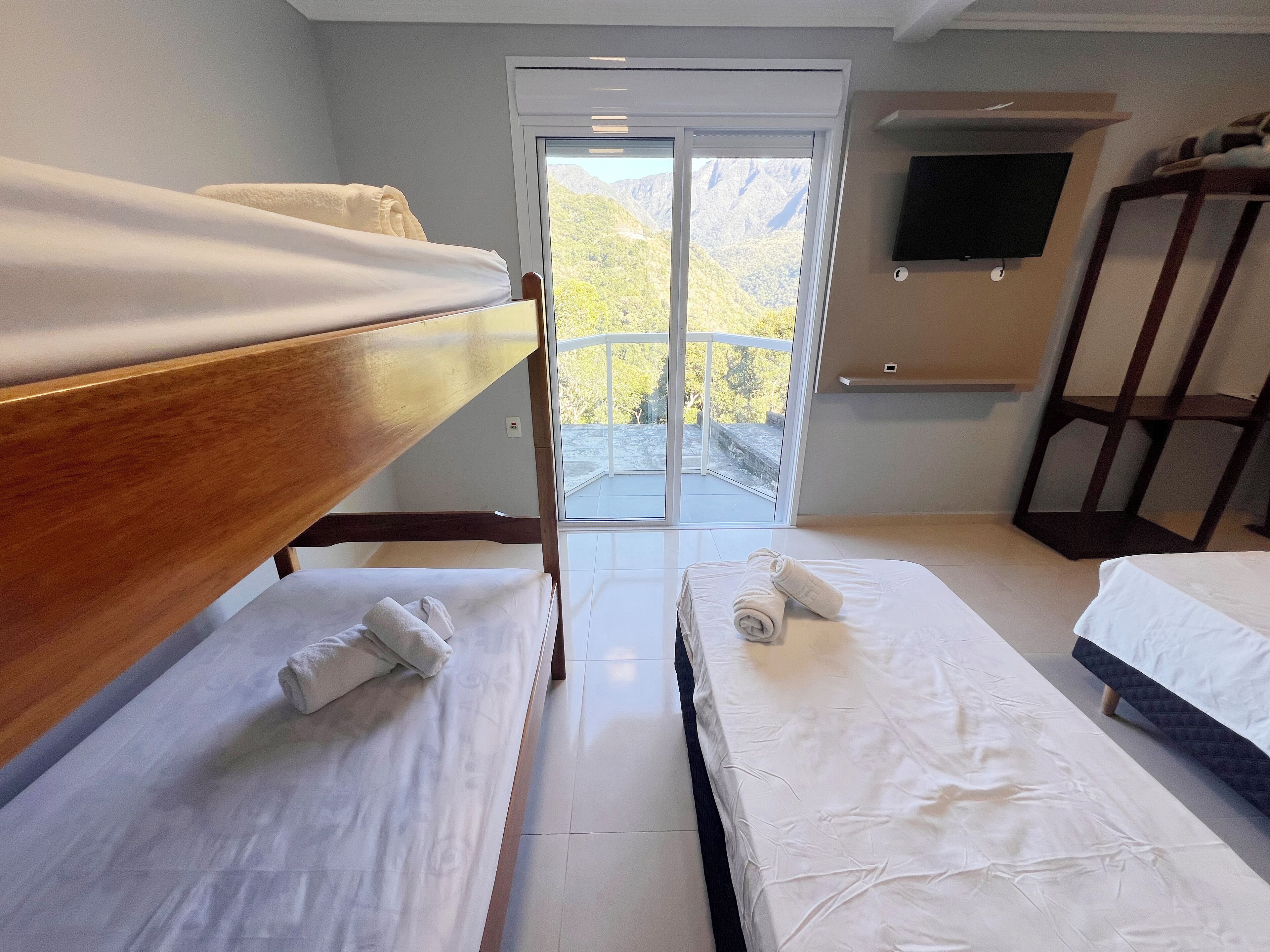A hotel room with two beds, a TV, and a balcony with a mountain view.