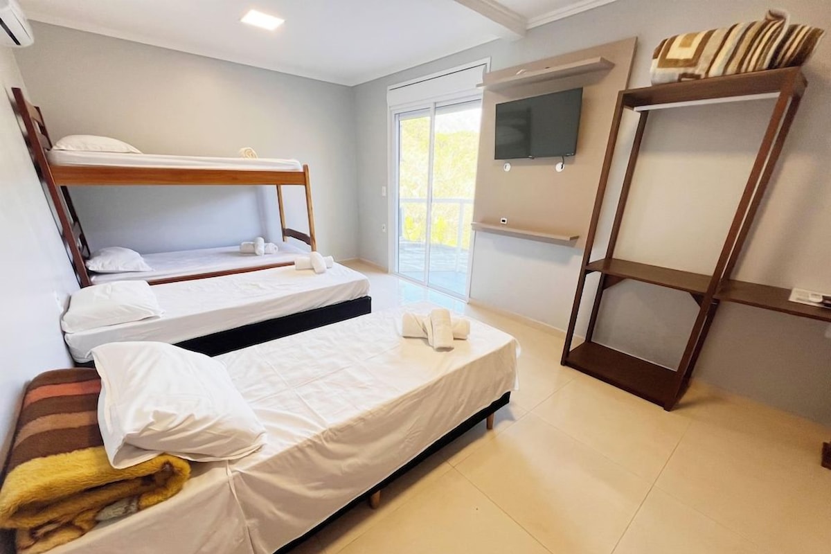 Habitación de hotel con dos camas literas, una cama plana, un televisor en la pared y una puerta corredera al exterior.