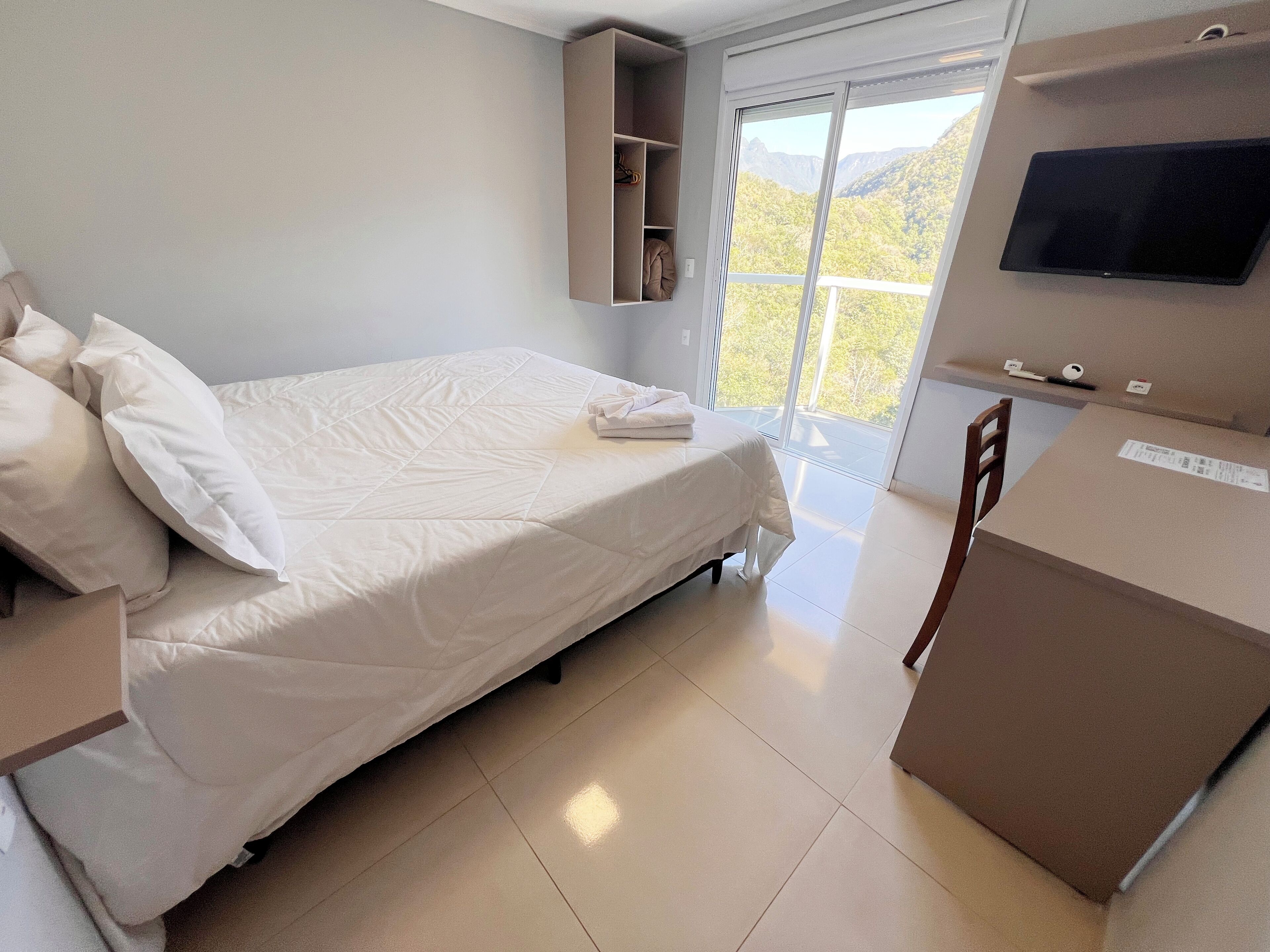A hotel room with a bed, a TV, a desk, and a view of the outdoors.