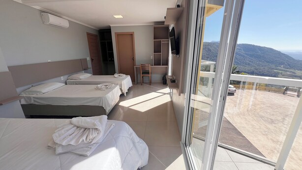 A hotel room with two beds, a desk, a chair, a TV, and a balcony with a view of the mountains.