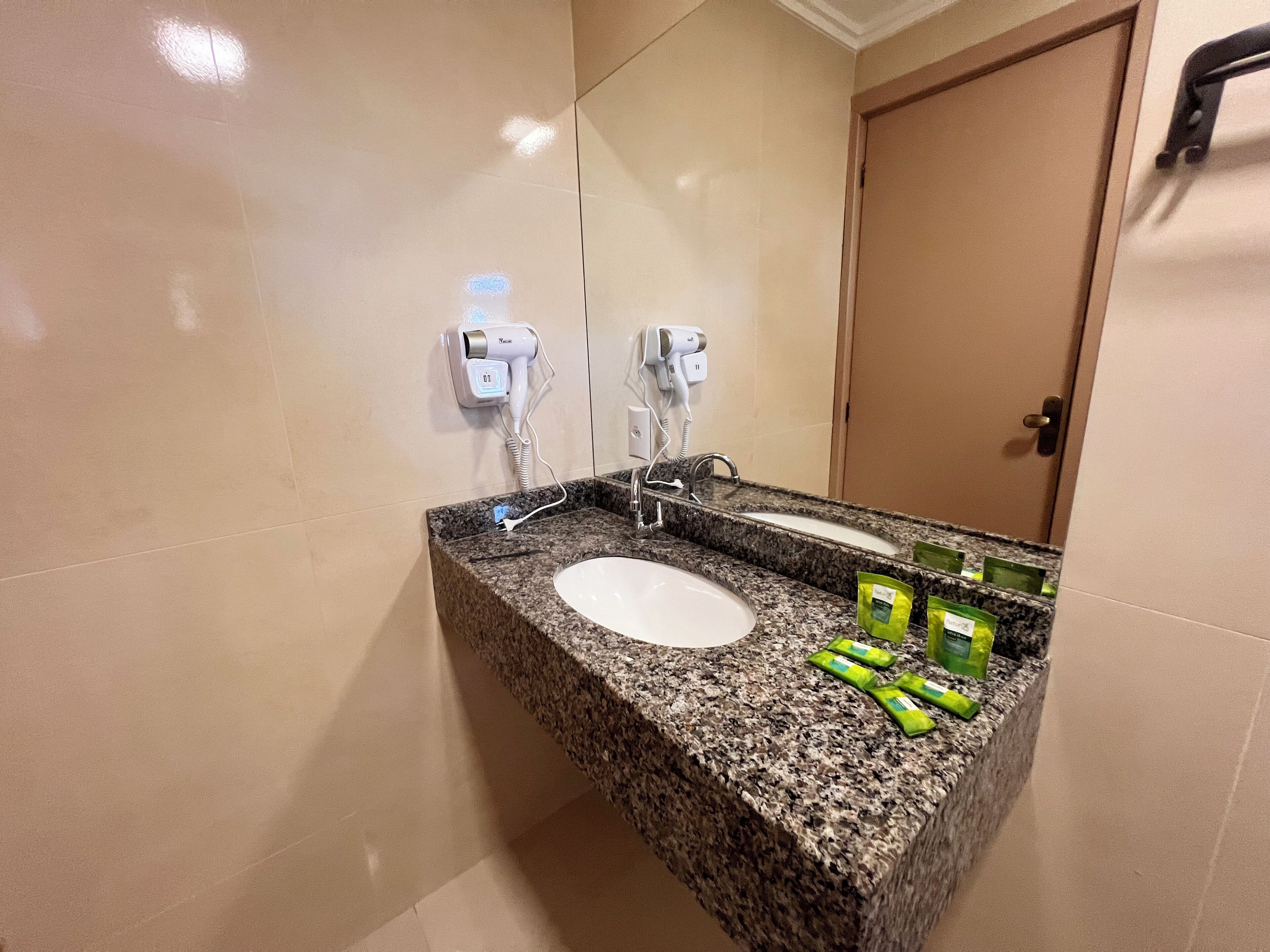 Een badkamer met een granieten aanrechtblad, een witte wastafel en twee haardrogerbeurten aan de muur.