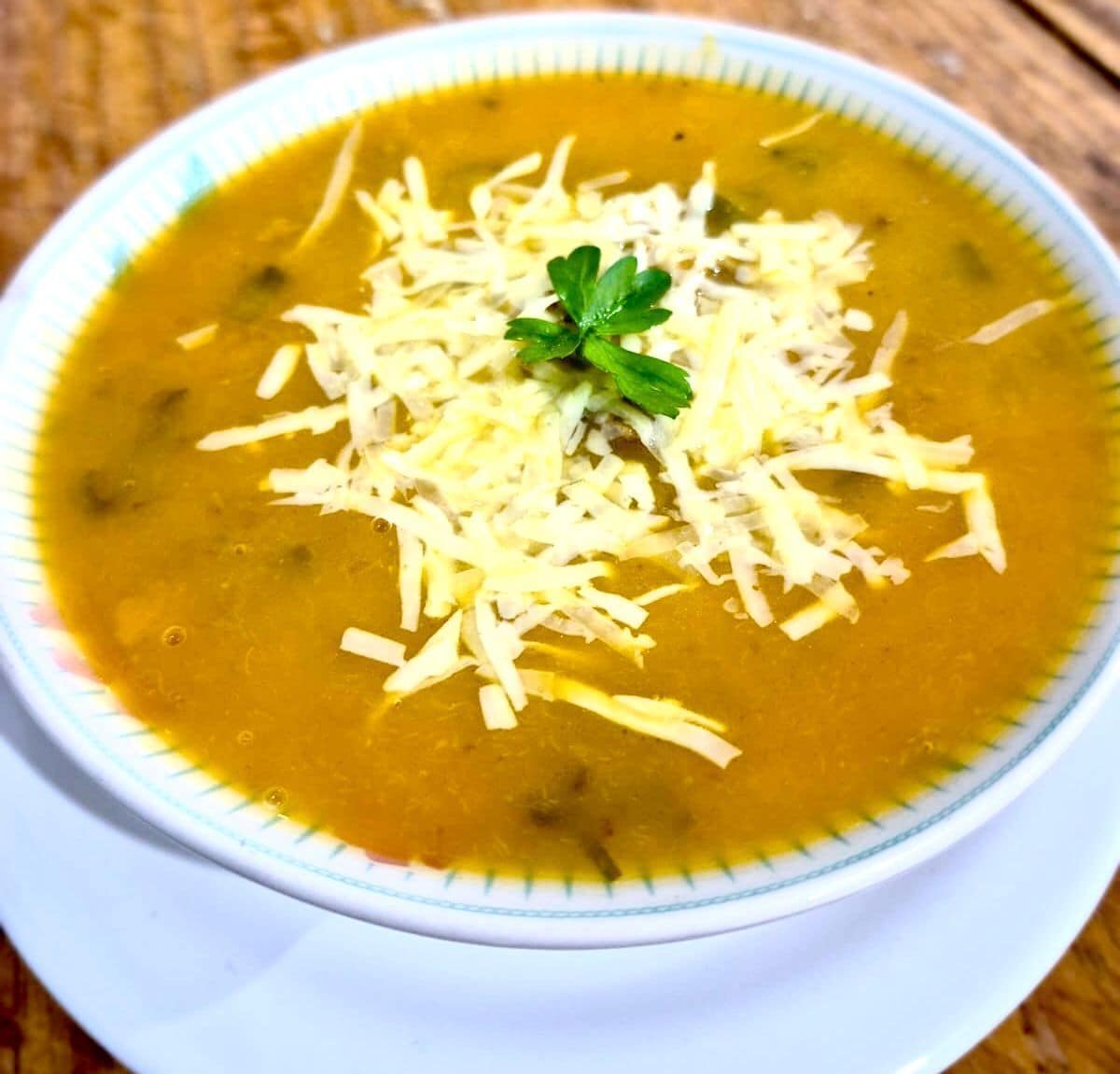 A bowl of soup with shredded cheese and a garnish on top.