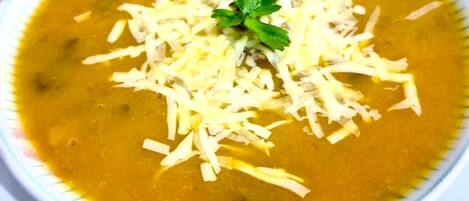 A bowl of soup with shredded cheese and a garnish on top.