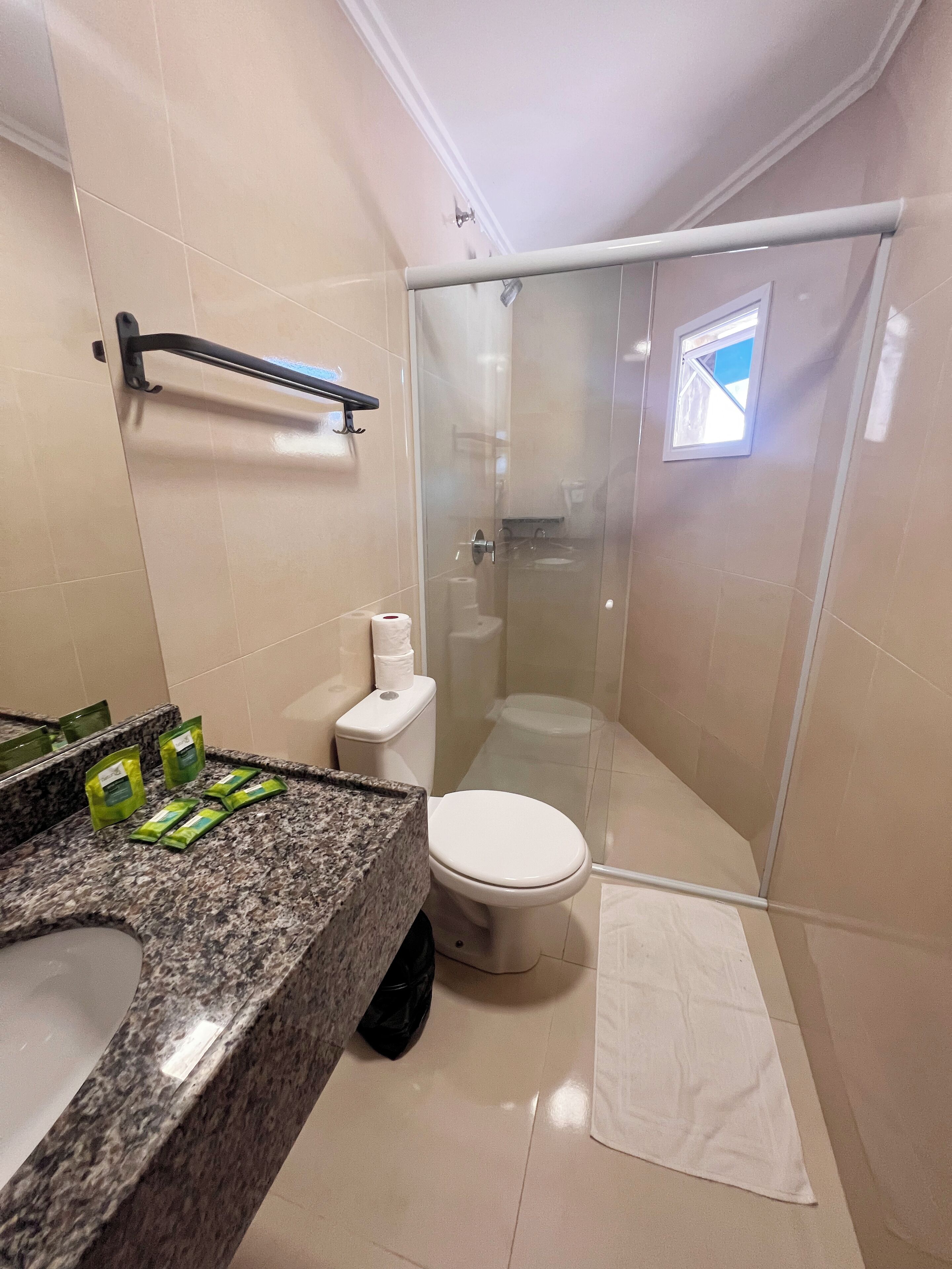 A bathroom with a granite countertop, a toilet, a glass shower enclosure, and a small window.