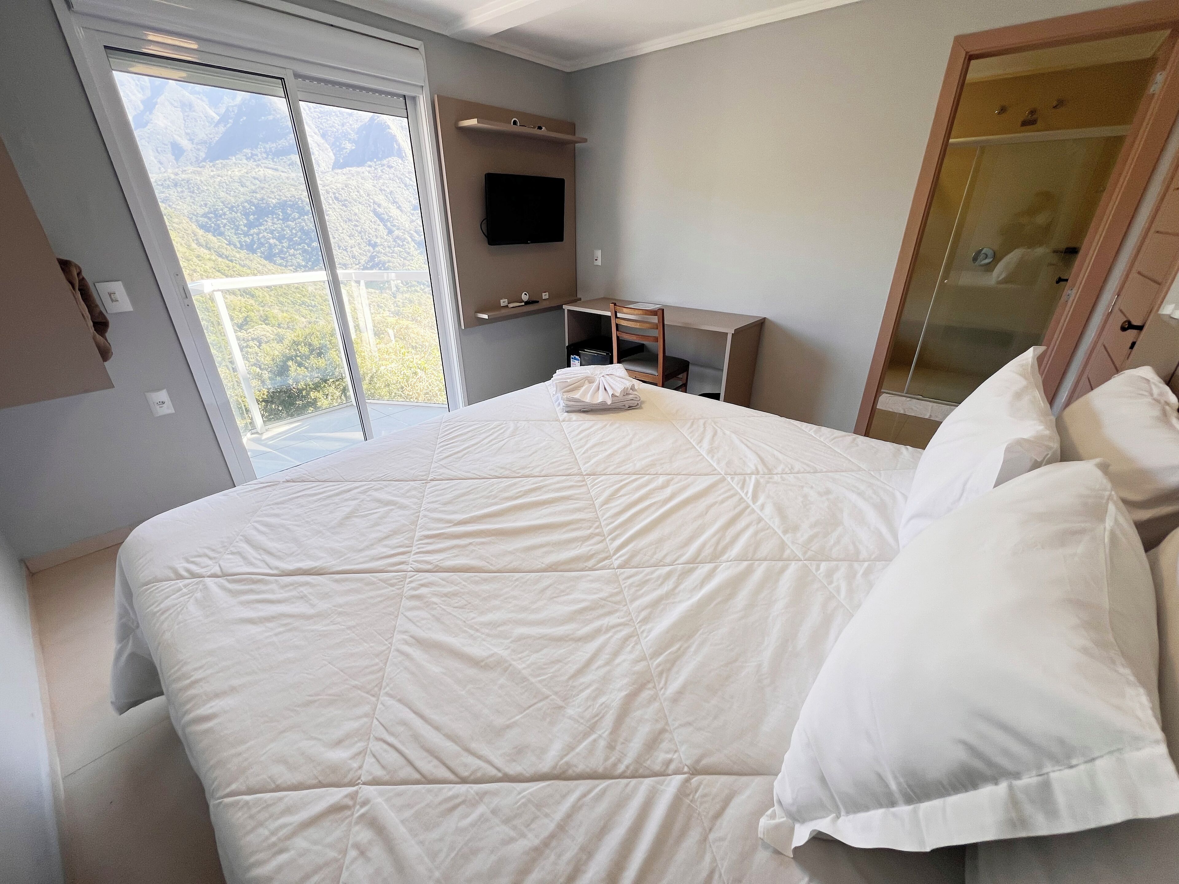Quarto com uma cama grande, televisão, escrivaninha e guarda-roupa.