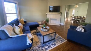A living room with a fireplace, a ceiling fan, and a dining area in the background. - King Suites - 2 King Beds & Garage Parking (Lakewood)