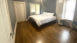 A bedroom with a bed, a ceiling fan, a window with blinds, and a small table with a lamp. - King Suites - 2 King Beds & Garage Parking (Lakewood)