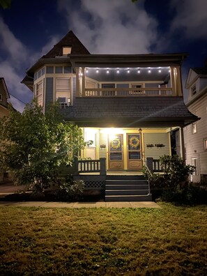 A two-story house with a front porch, steps, and a small garden area. - King Suites - 2 King Beds & Garage Parking (Lakewood)