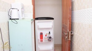 A narrow hallway with a refrigerator and a coffee maker on the left, and a door on the right. - Stay.Plus Royale Village Apartment (Syokimau)