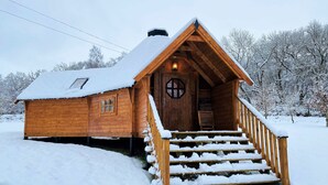 A wooden cabin with a snow-covered roof, a wooden staircase leading to the entrance, and a snow-covered landscape.