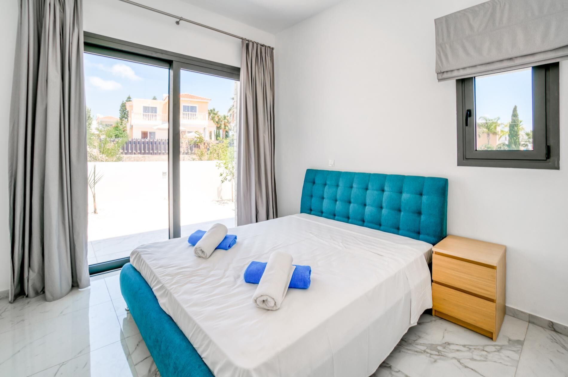 A hotel room with a large bed, a wooden nightstand, and a window with a view of buildings and trees.