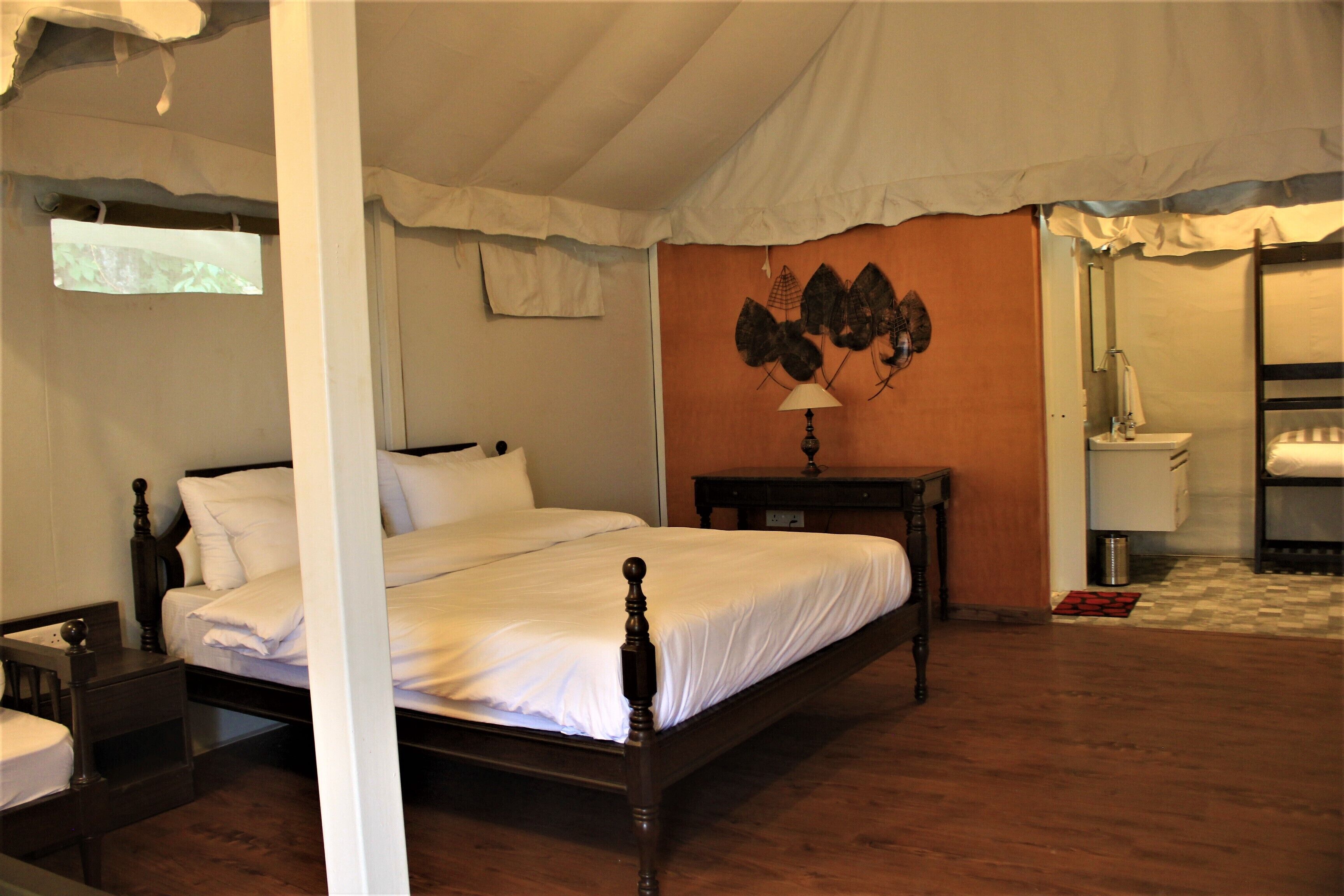 A bedroom with a four-poster bed, a nightstand, a bedside table, a wall-mounted lamp, and a bathroom with a sink and mirror.