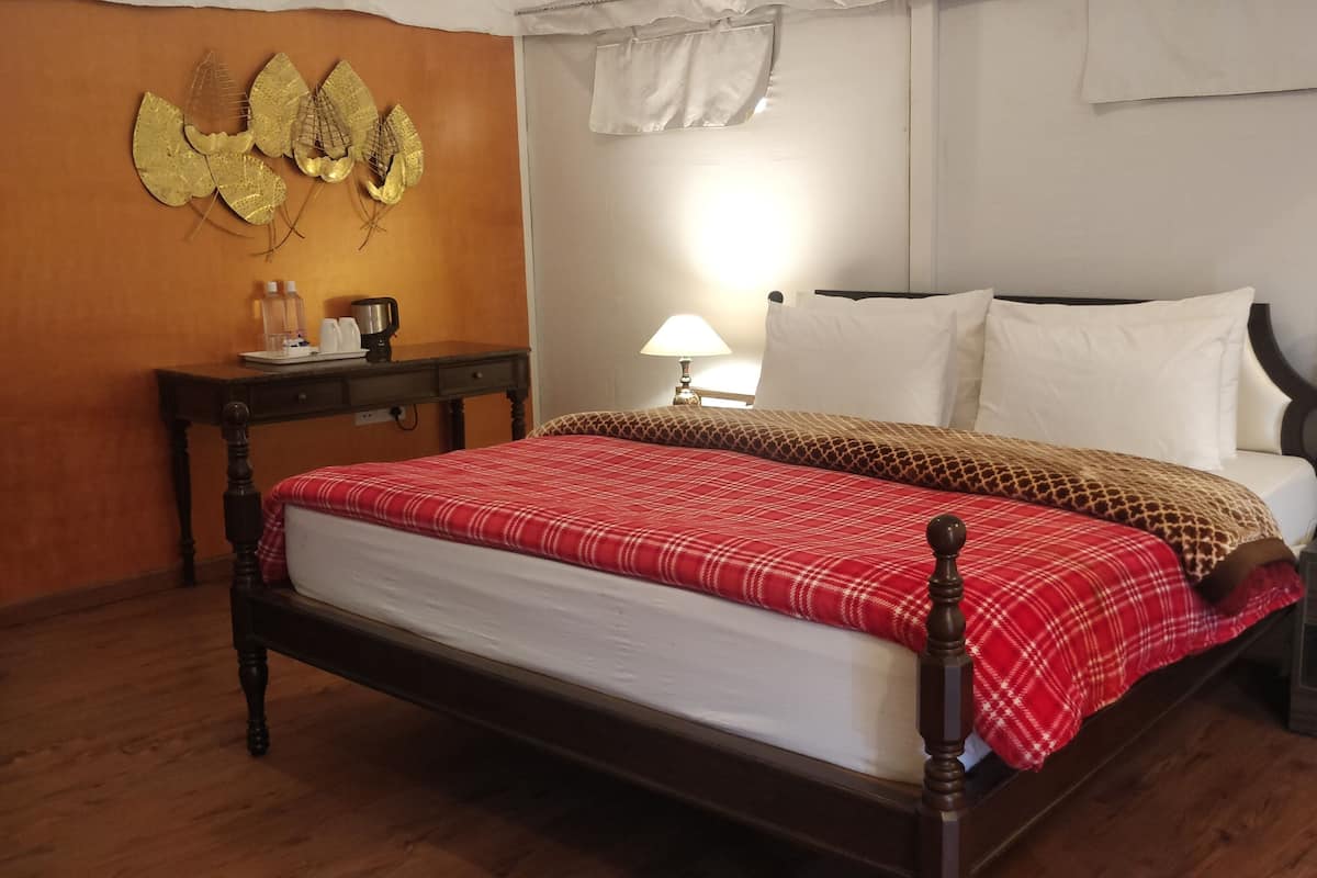 Habitación de hotel con una cama de madera, una colcha roja escocesa, una mesita de noche con una lámpara y un adorno en la pared.