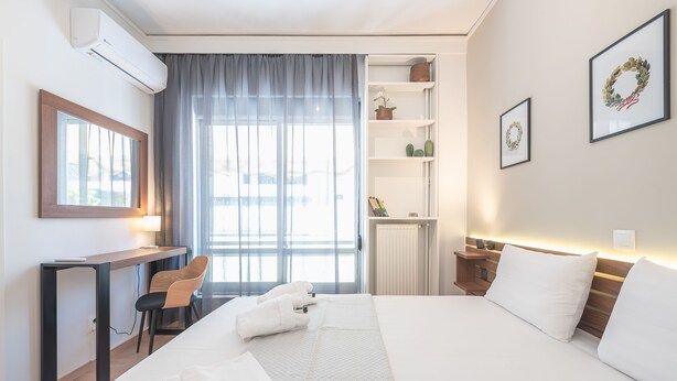 Ein Hotelzimmer mit einem Bett, einem Schreibtisch, einem Stuhl, einem Fenster mit Vorhängen und einem Regal mit Dekoration.