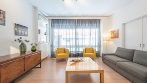 Ein modernes Wohnzimmer mit einem Holztisch, zwei gelben Armstühlen, einem grauen Sofa und einer Holzkassette mit dekorativen Schnitzereien.