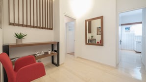 Ein moderner Empfangsbereich mit einem roten Sessel, einem hölzernen Regal mit Pflanze und einem wandmontierten Spiegel.