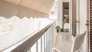 Ein Balkon mit weißer Reling, einem kleinen Tisch mit Topfpflanze und einem Stuhl.