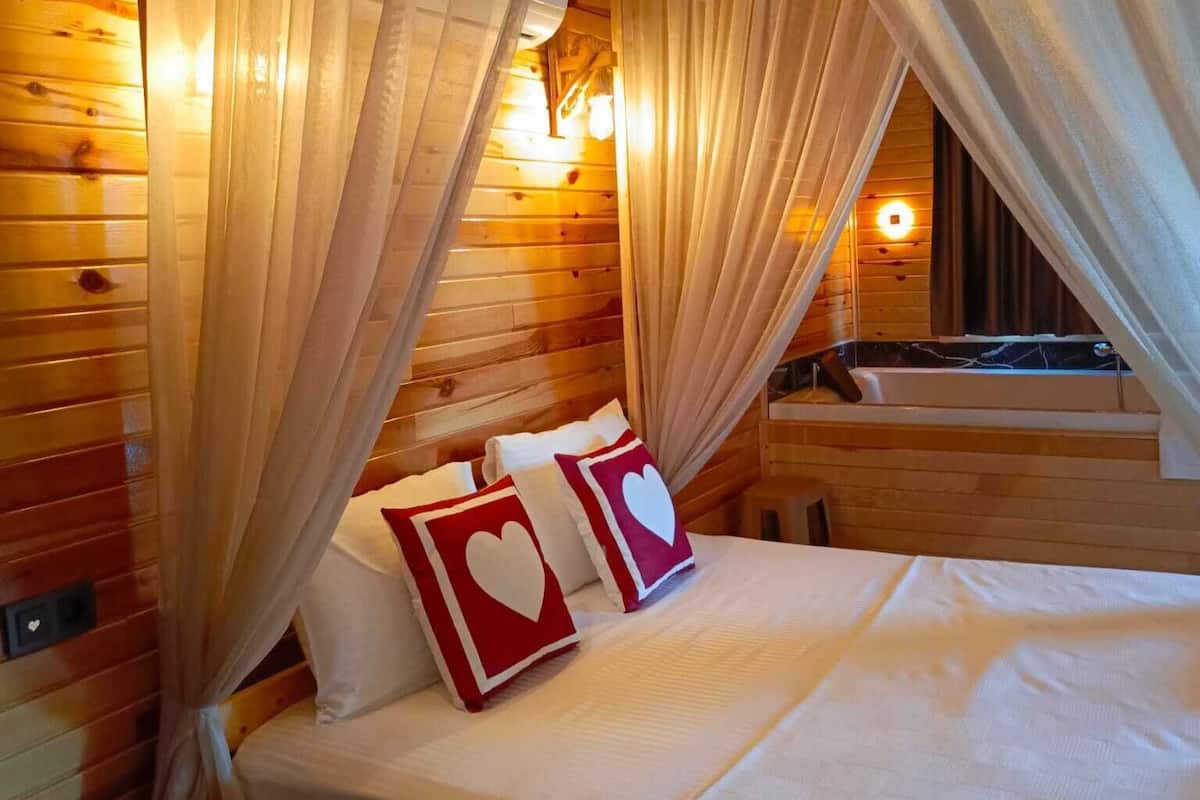 A wooden cabin room with a bed, two heart-shaped pillows, and a bathtub.
