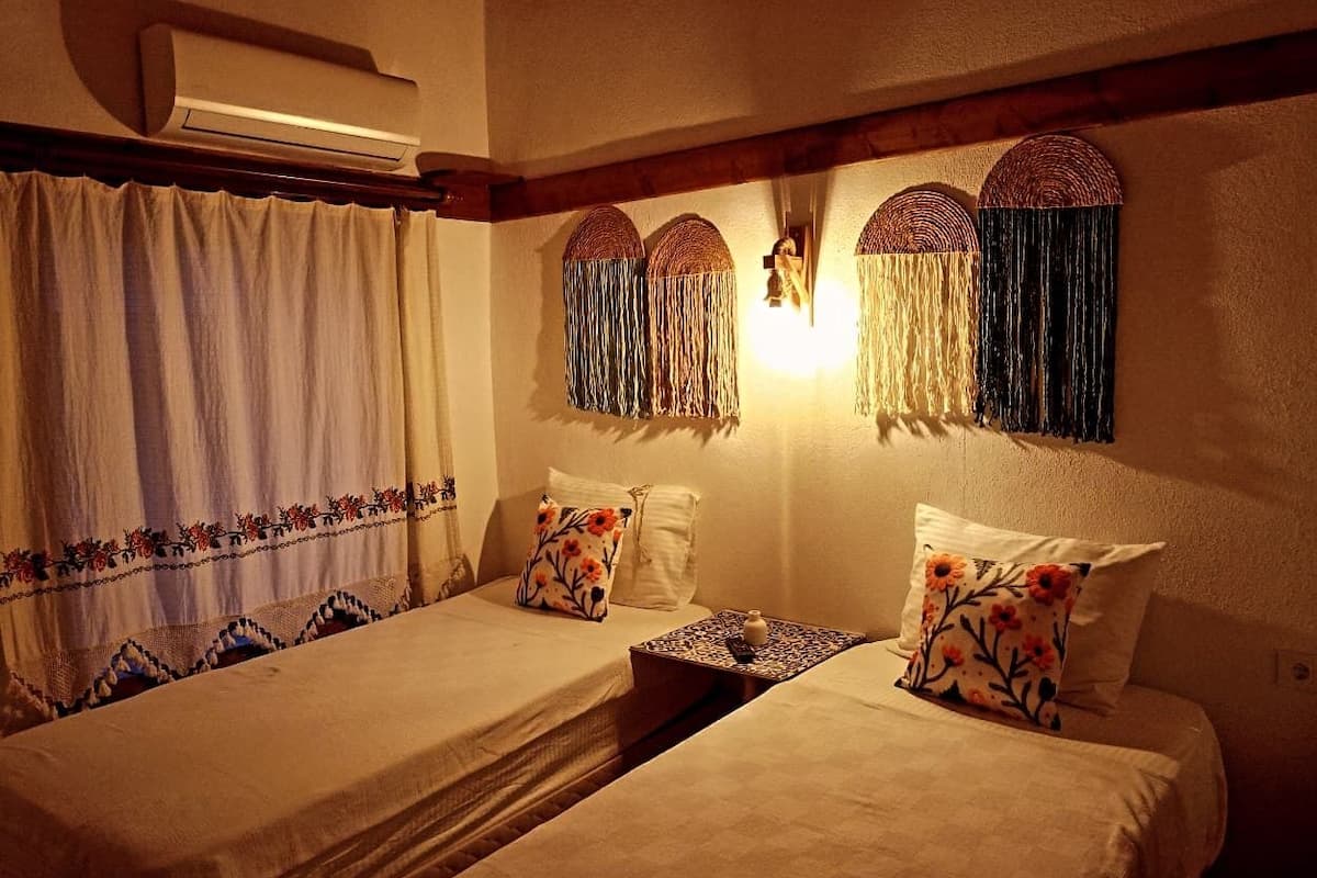 A room with two beds, a wall-mounted air conditioner, and decorative wall hangings.
