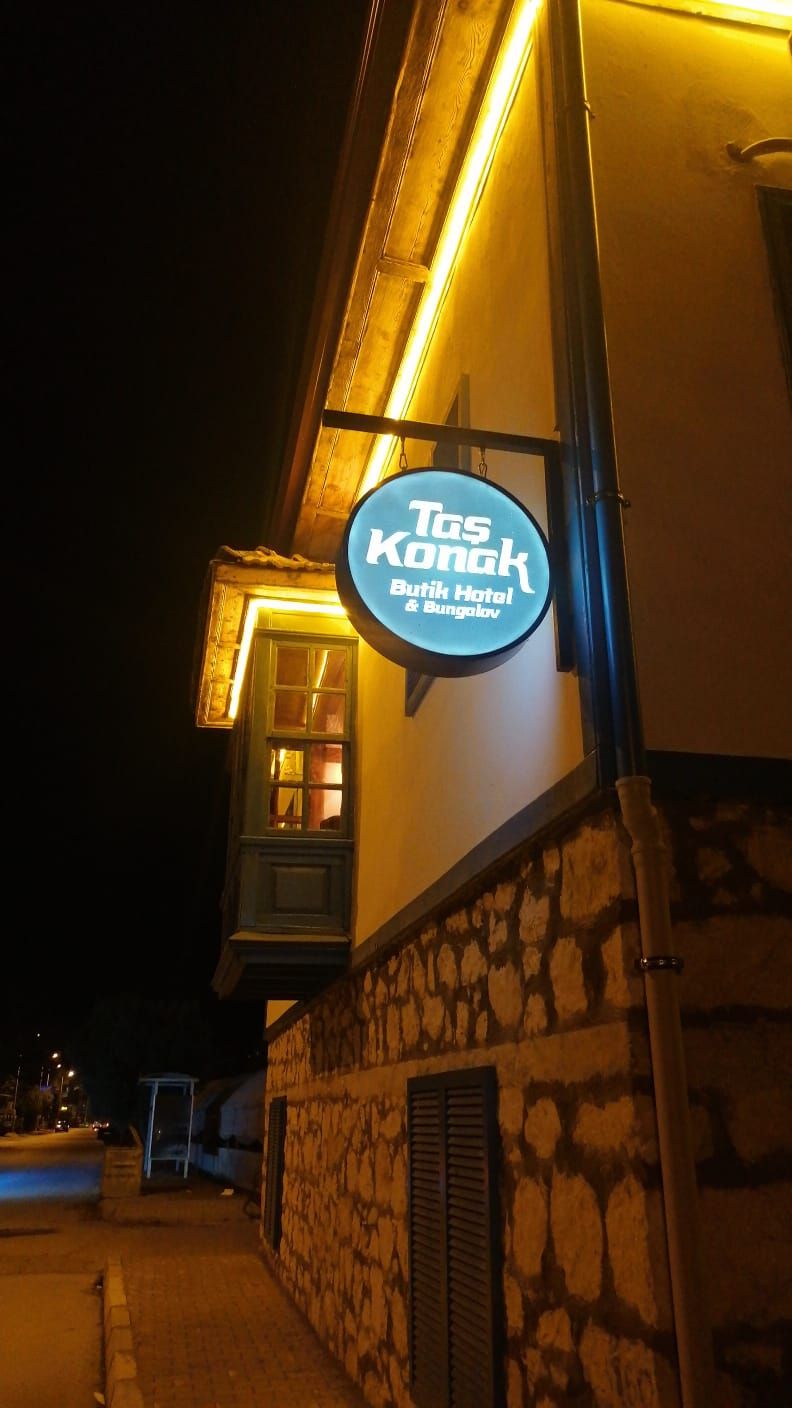 Une enseigne d’hôtel portant le nom « Tas Konak Butik Hotel & Bungalow », illuminée la nuit.