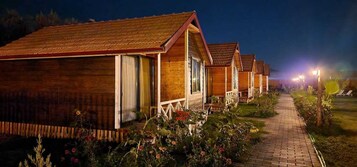 Una hilera de cabañas de madera con un sendero de ladrillo que las conecta, rodeadas de jardines cuidados.