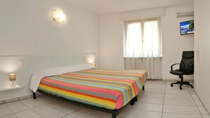 Una camera d'albergo con un letto, una sedia, una televisione e una finestra con tende.