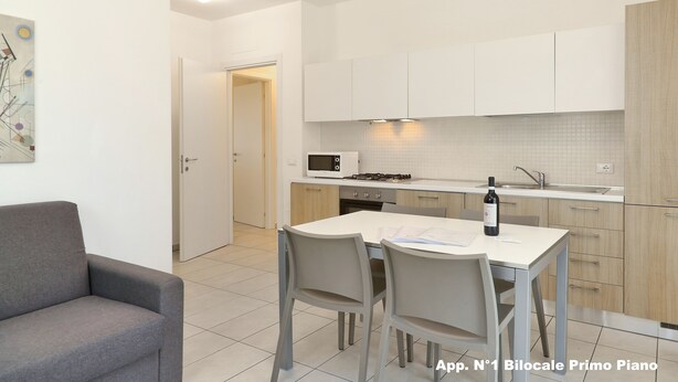 Una cucina moderna con mobili bianchi, un tavolo da pranzo con sedie e un divano in un soggiorno.