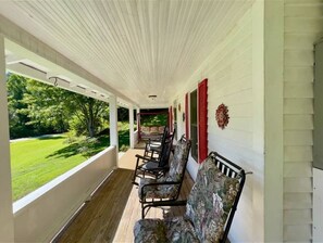 A covered porch with wooden flooring, a row of chairs, and a view of a green landscape. - O'Henry's Getaway, on Cheoah River (Robbinsville)