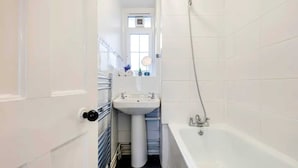 Ein schmales Badezimmer mit einem weißen Waschbecken, einem Spiegel und einer Badewanne.