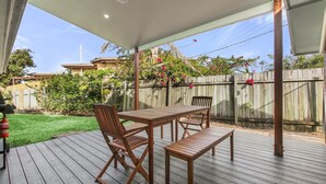 A covered patio with a wooden table and chairs, surrounded by a wooden fence and greenery. - Bell Street 36, Dicky Beach (Dicky Beach)
