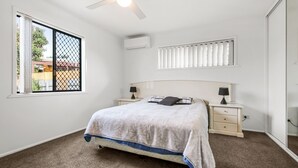 A bedroom with a bed, bedside tables, a window with a view, an air conditioning unit, and a ceiling fan. - Bell Street 36, Dicky Beach (Dicky Beach)