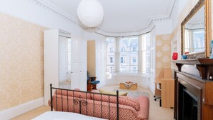 Une chambre à coucher comprenant un lit, un canapé, une cheminée et une grande fenêtre donnant sur des immeubles.