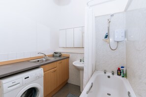 A modern bathroom with a washing machine, sink, and bathtub.