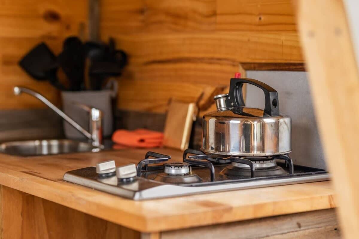 Una cocina compacta con estufa de gas portátil, hervidor y pileta.