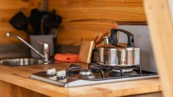 Una cocina compacta con estufa de gas portátil, hervidor y pileta.