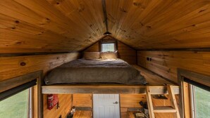 A cozy attic bedroom with a loft bed, wooden walls, a small window, and a door.