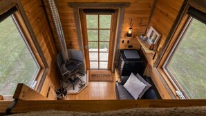 A cozy cabin interior with a wooden interior, a fireplace, a sofa, and a small table with a lamp.