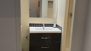 A bathroom with a white sink, dark vanity, and a mirror above it. - Appartement MTM (Montpellier)