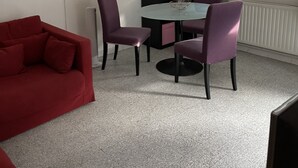 A room with a red sofa, a dining table with four chairs, and a window with blinds. - Appartement MTM (Montpellier)