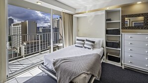 A modern hotel room with a balcony, a bed with a patterned bedspread, a dresser, and a large mirror. - Ocean & Iconic Waikiki Views from the Marine Surf by the Beach w/Full Kitchen (Honolulu)